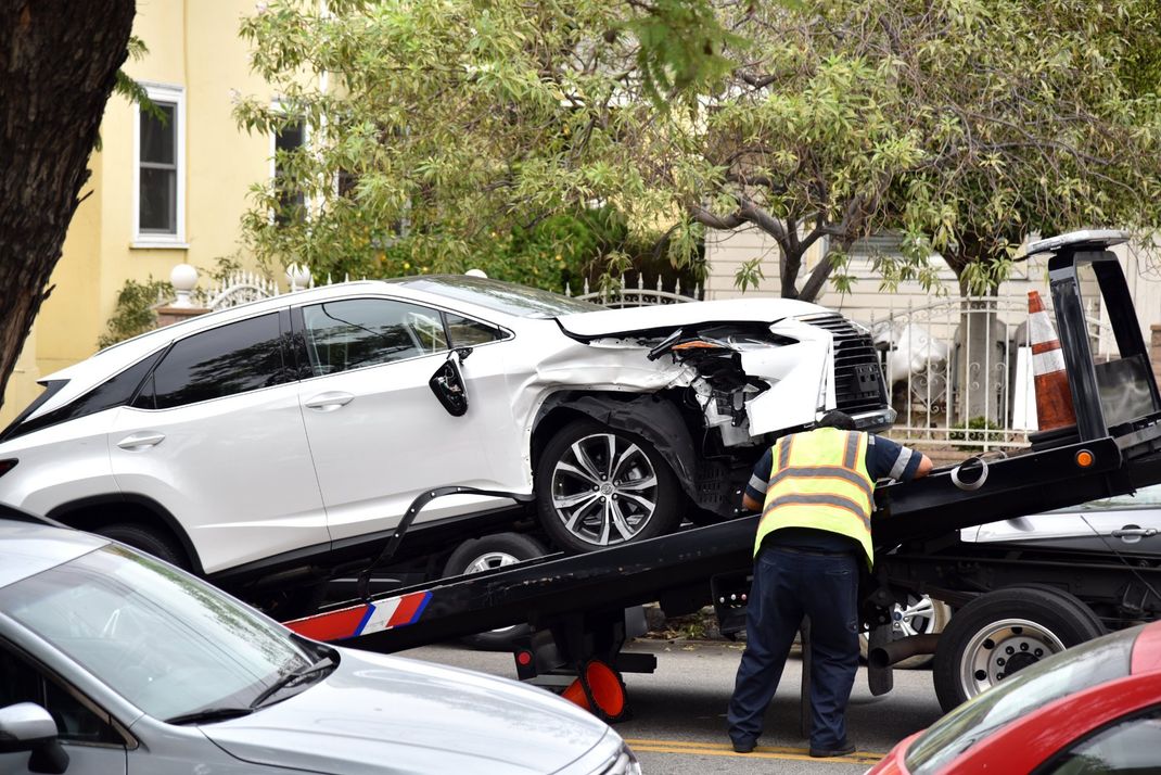 Un operatore di carro attrezzi carica un SUV bianco incidentato con danni posteriori su un pianale in strada.
