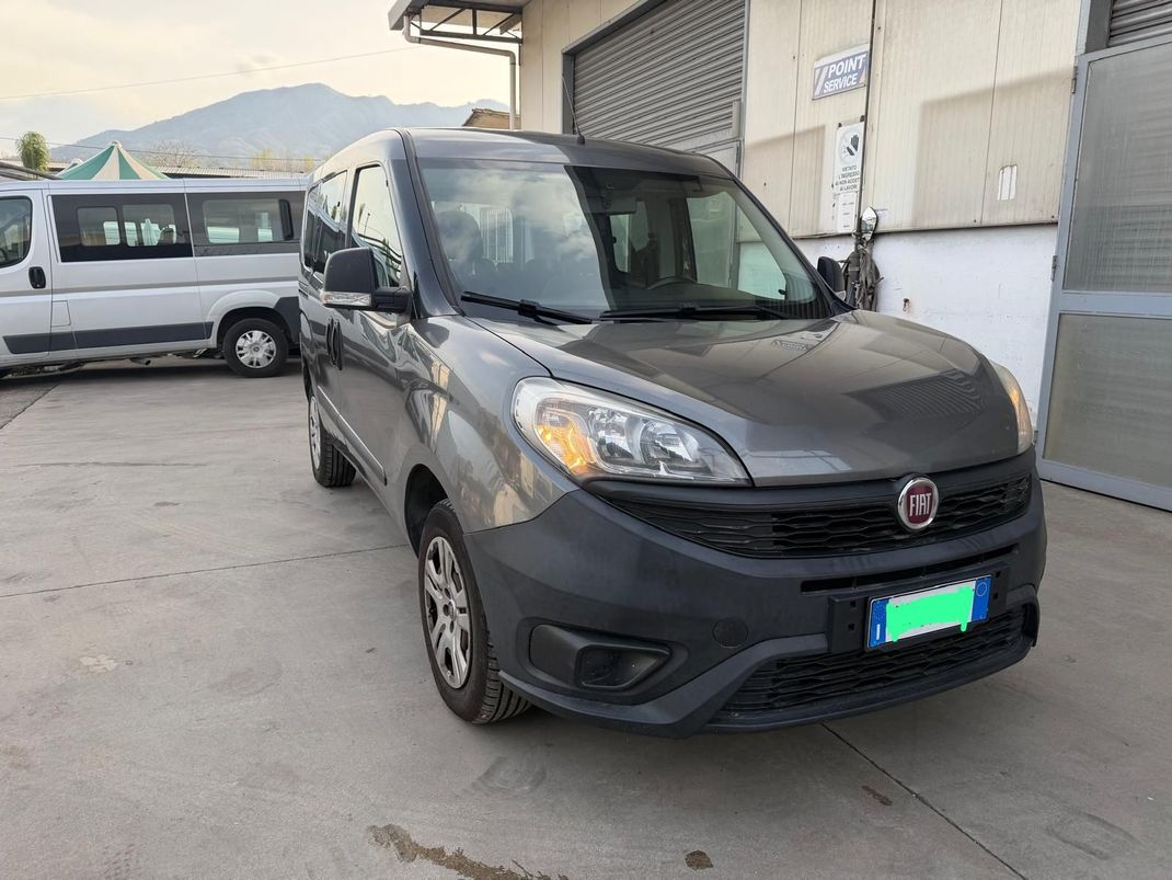 Un furgone grigio scuro è parcheggiato fuori da un magazzino, con un altro furgone bianco sullo sfondo.