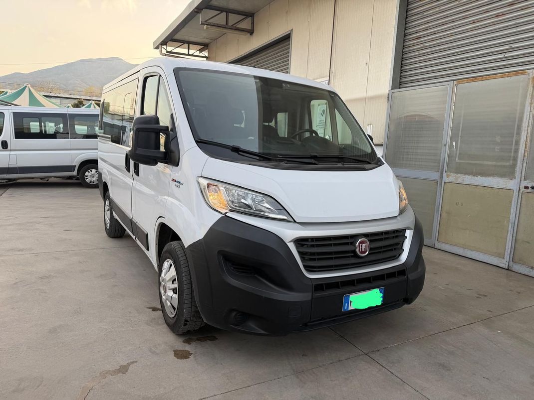 Furgone Fiat bianco parcheggiato davanti a un edificio, vista frontale su un piazzale asfaltato.