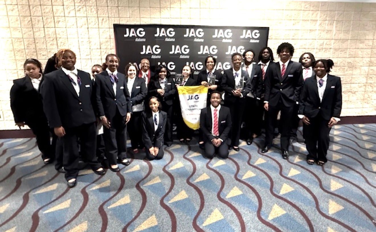 Group in formal attire posing in front of a JAG backdrop at an indoor event
