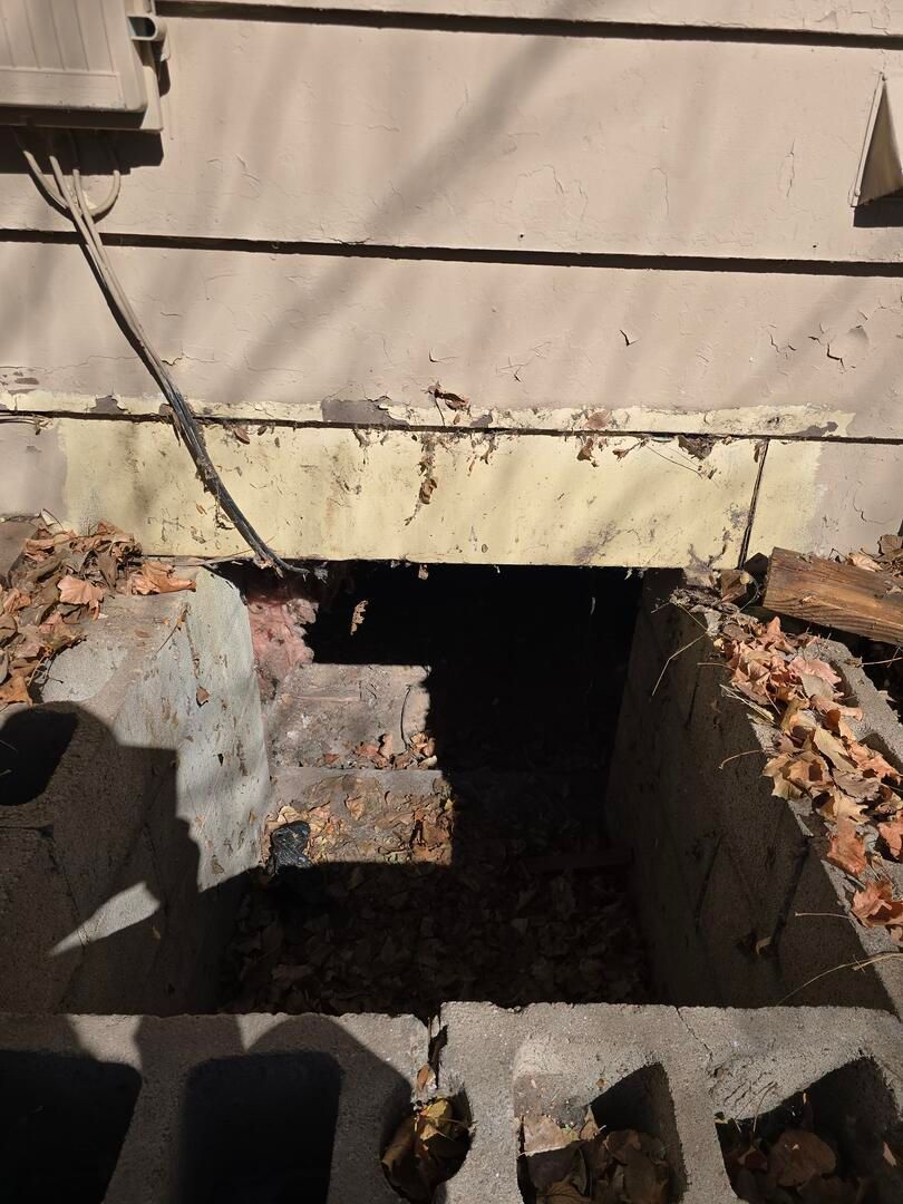 Basement excavation beside a house foundation with exposed concrete and dirt walls.