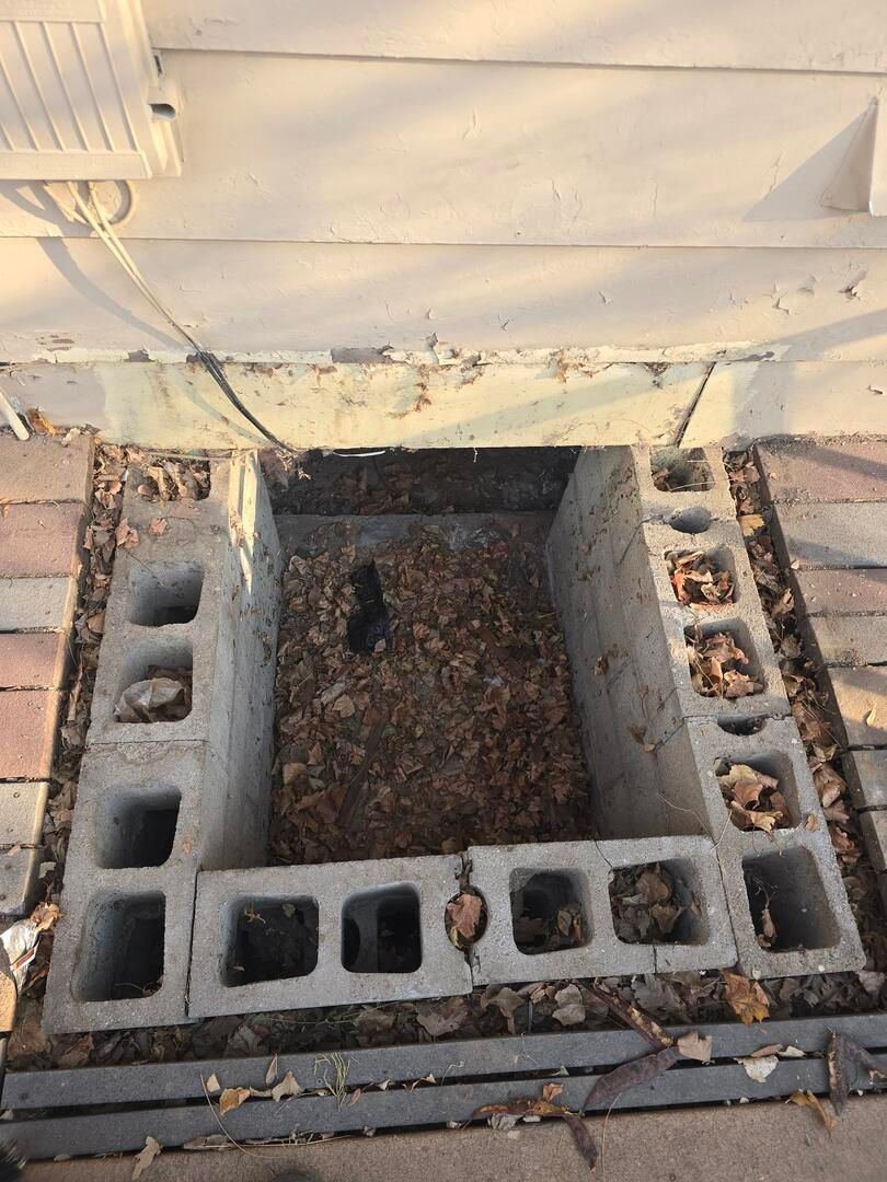 Concrete cinder block pit with debris and an open cavity beside a house wall