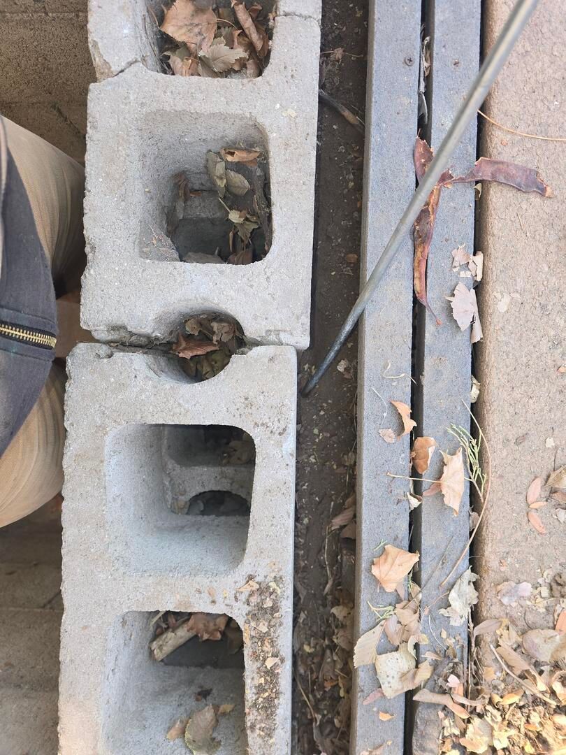 Stacked gray cinder blocks beside a metal bench, with leaves and small debris on the ground.
