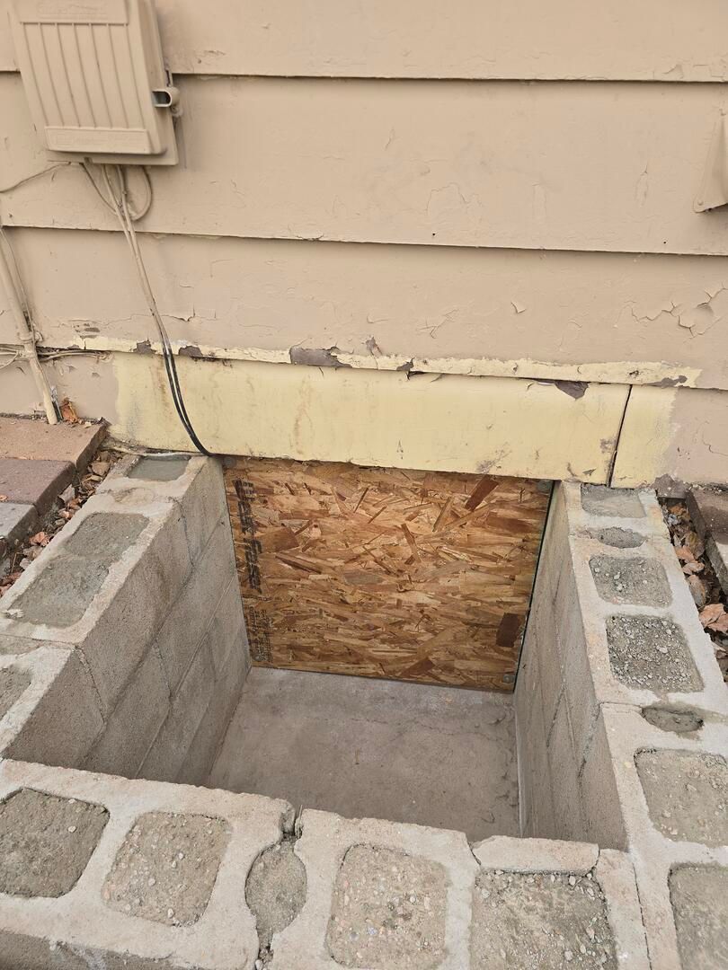 Damaged crawlspace opening under house with exposed plywood and cinder block border