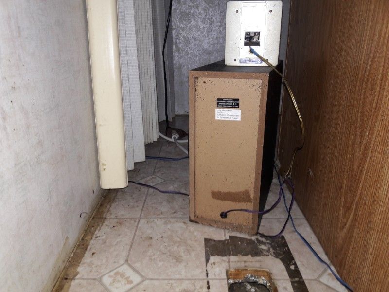 Speaker system in a cluttered, aged room. Brown speaker cabinet with a smaller white speaker on top, various wires.