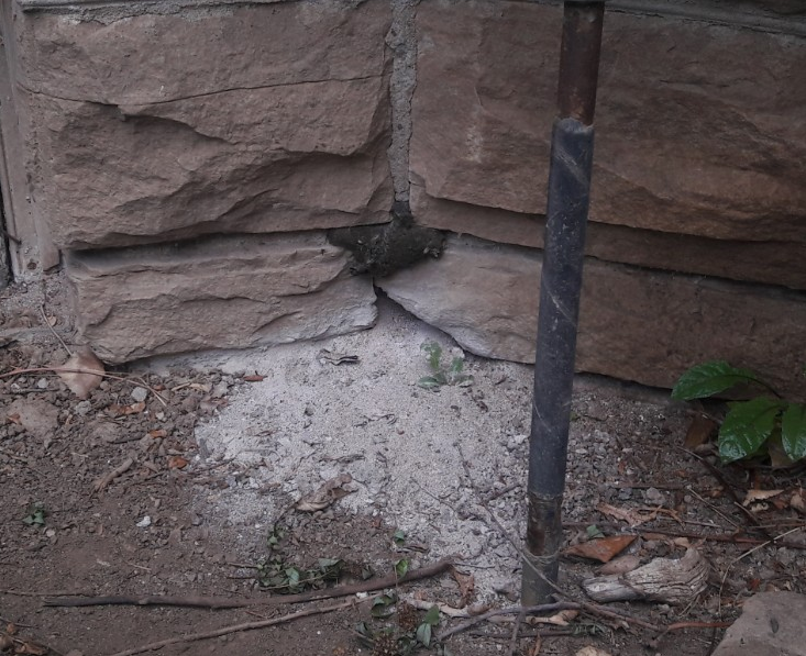 Stone building corner with dry, light-colored sand-like substance at base. Dark metal pole in front.