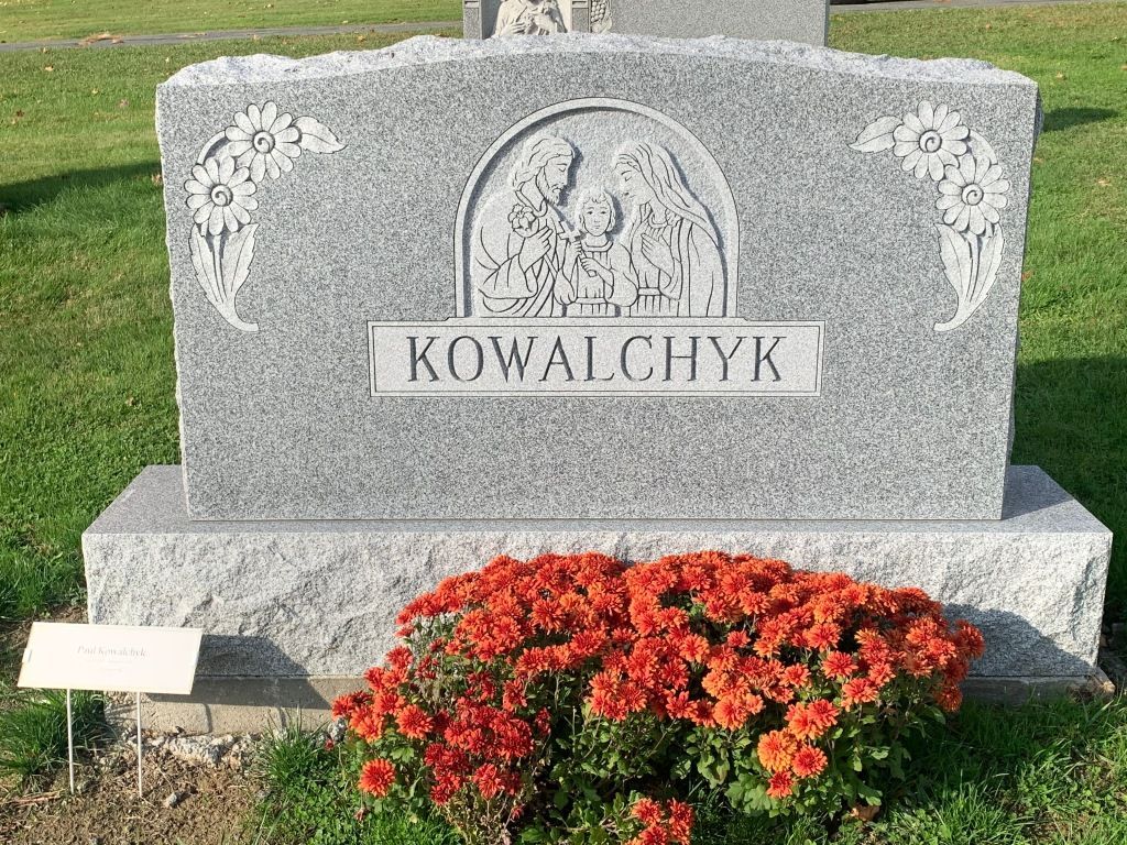 A gravestone in a cemetery with flowers in front of it.