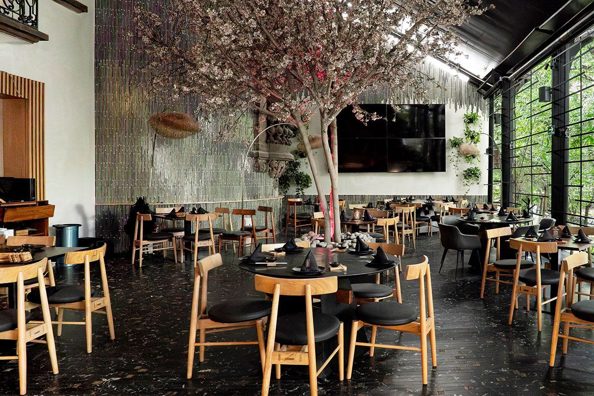 Interior de restaurante moderno con mesas de madera, sillas naranjas y grandes paredes con espejos.