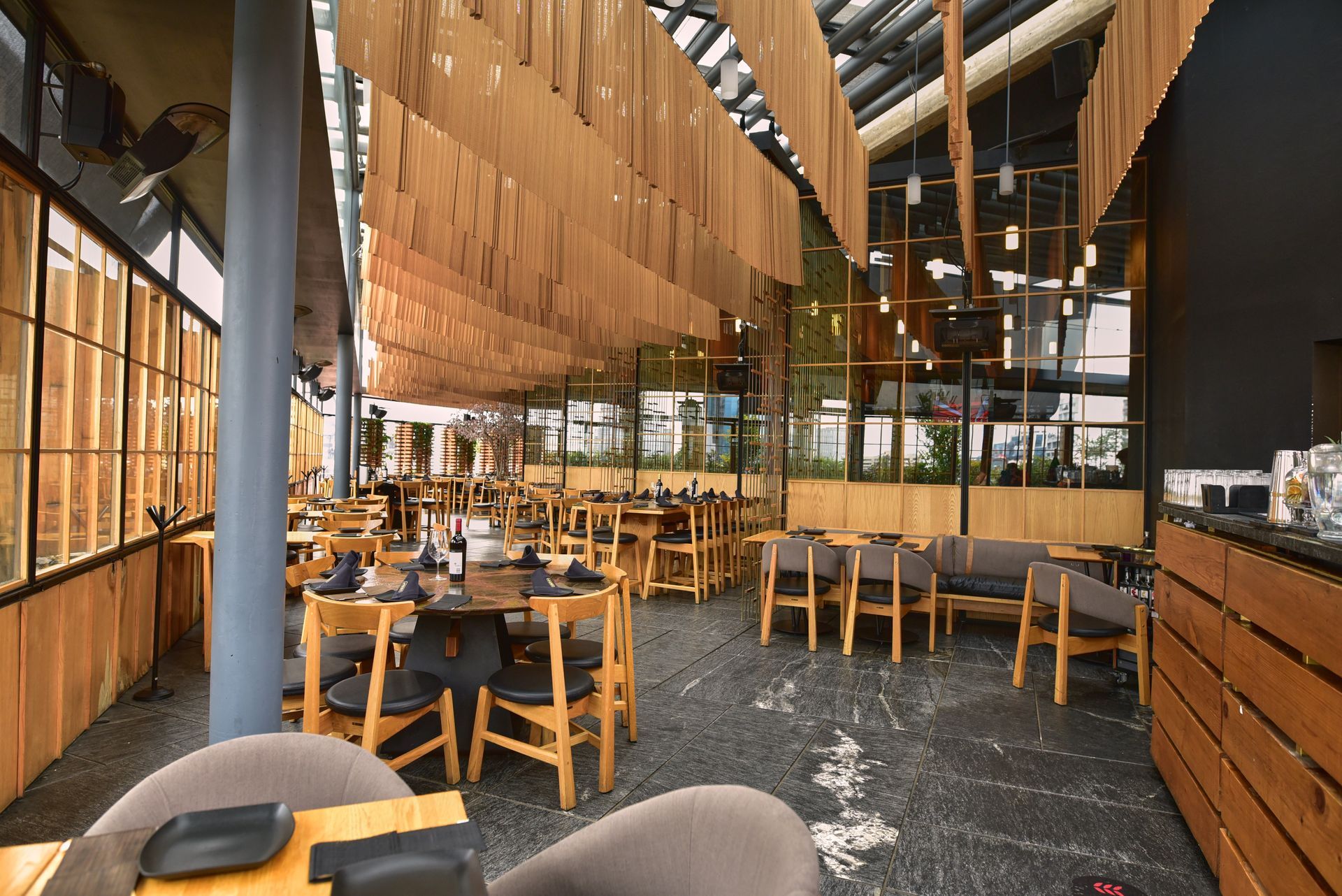 Interior de restaurante moderno con mesas y sillas de madera y una cálida decoración colgante bajo un techo alto.