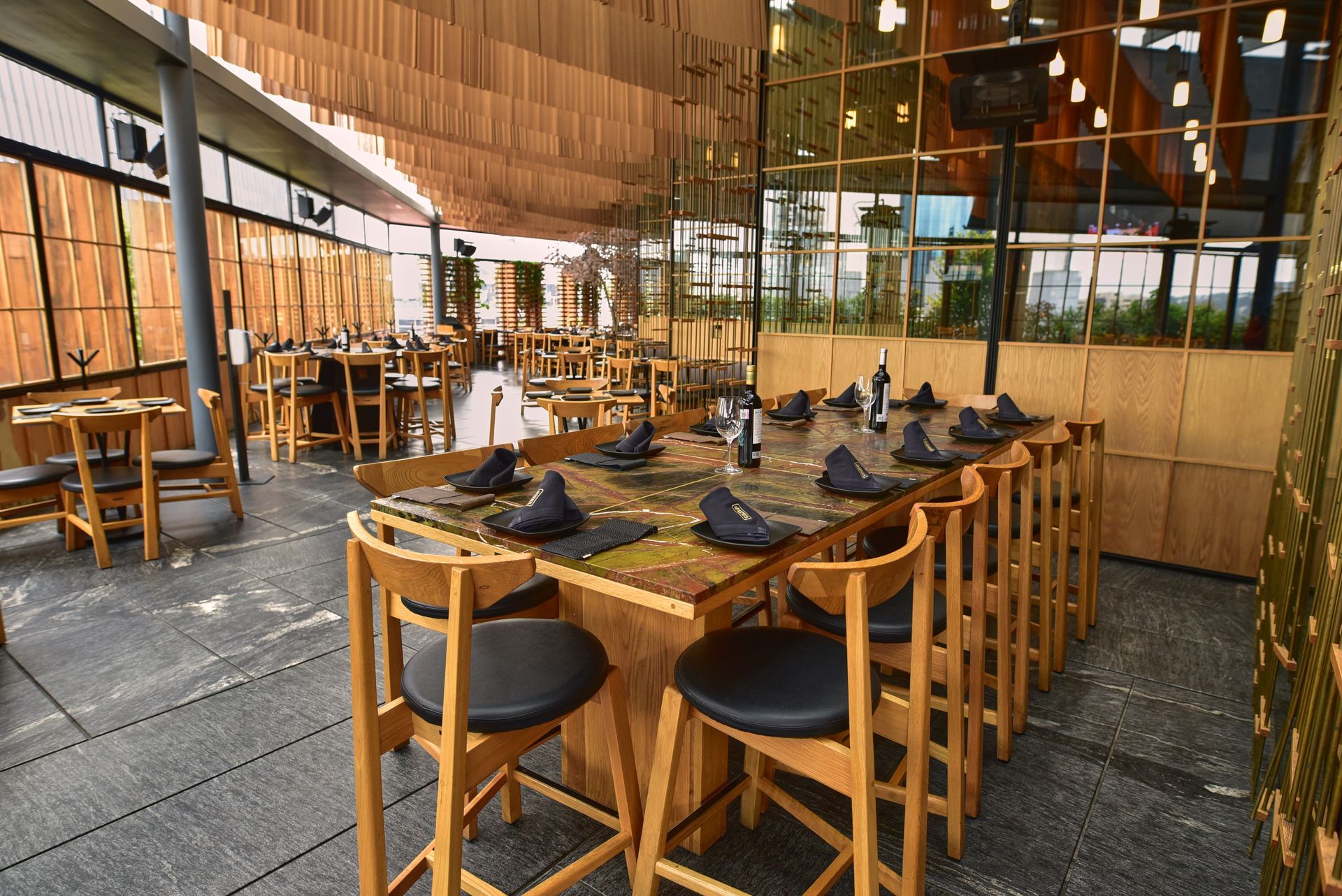 Mesas y sillas de madera en una moderna terraza de restaurante con paredes de cristal.