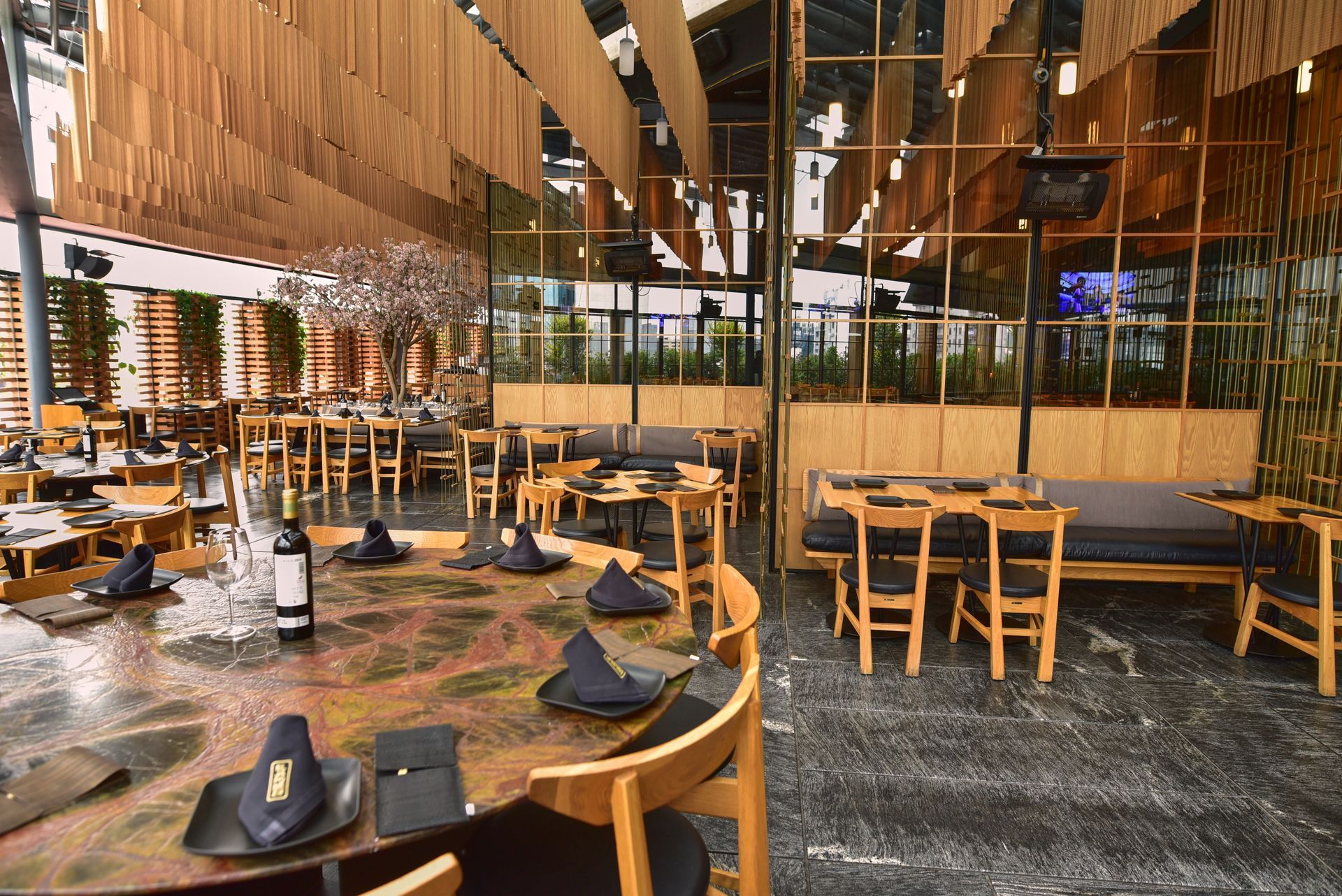 Interior de restaurante moderno con mesas y sillas de madera, y lámparas colgantes bajo un techo alto.