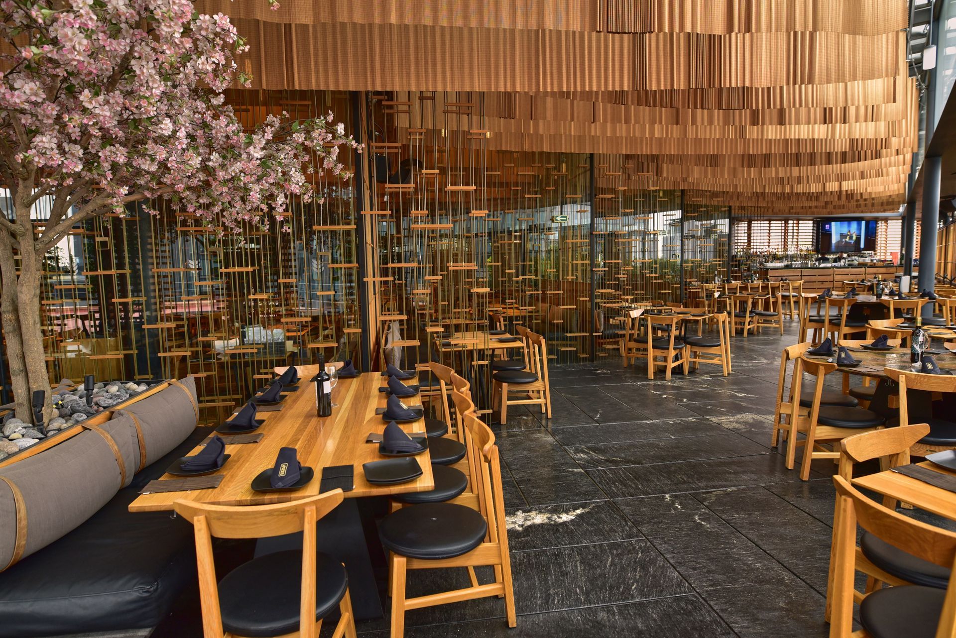 Comedor de restaurante moderno con mesas y sillas de madera, decoración floral e iluminación cálida.