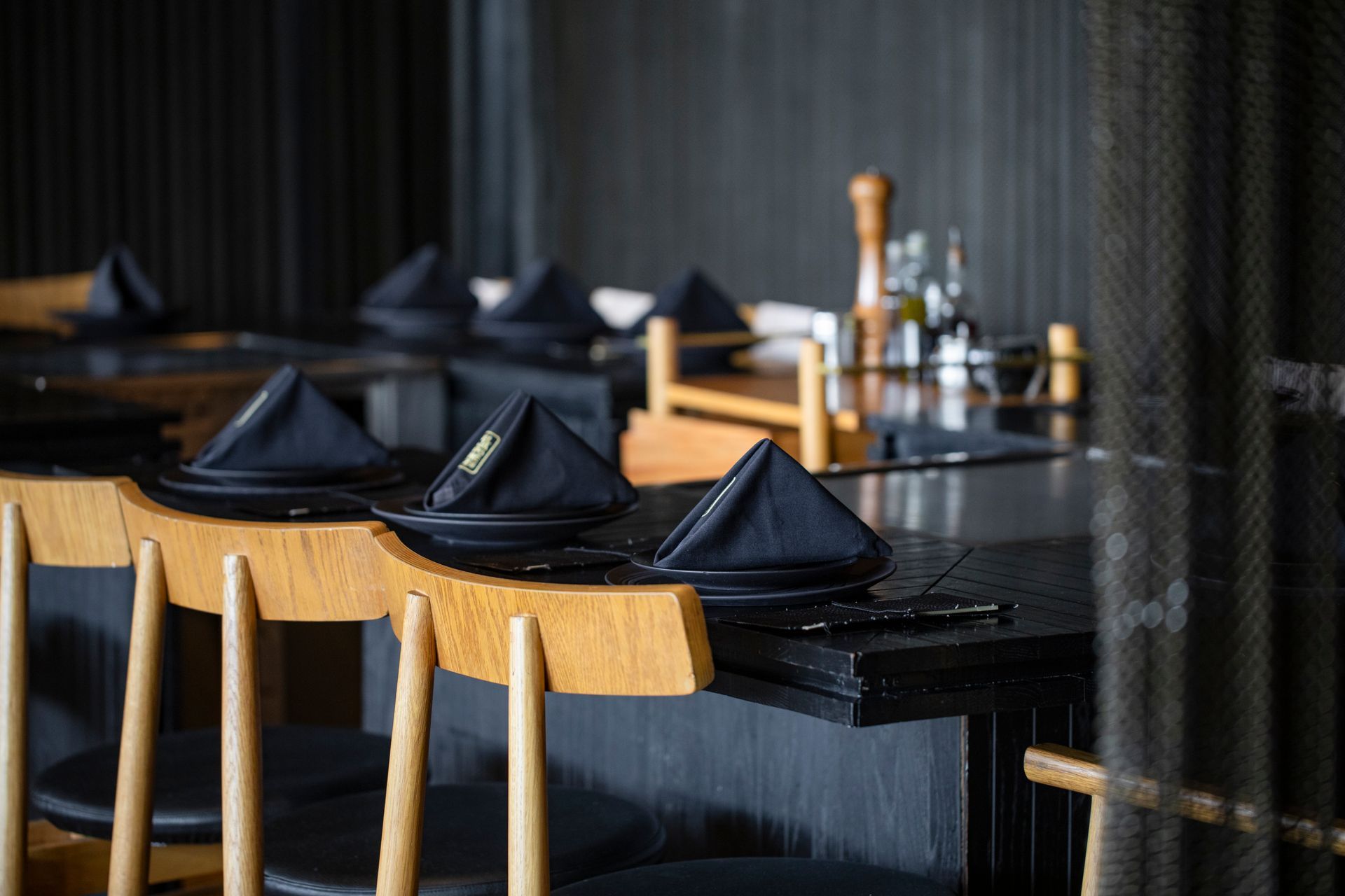Preparar la mesa del comedor con servilletas negras, sillas de madera y vajilla oscura en un restaurante con poca luz.