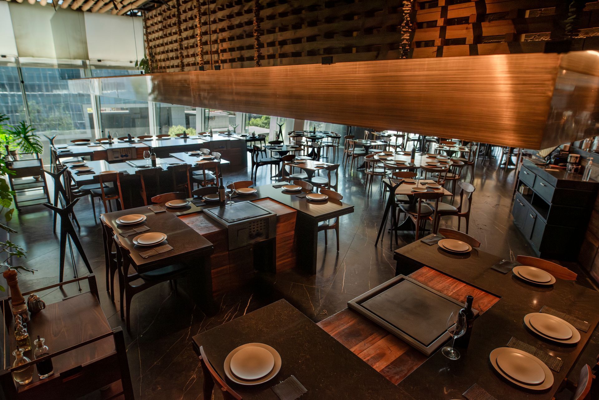 Comedor de restaurante moderno con mesas de madera, vajilla y una iluminación ambiental cálida.