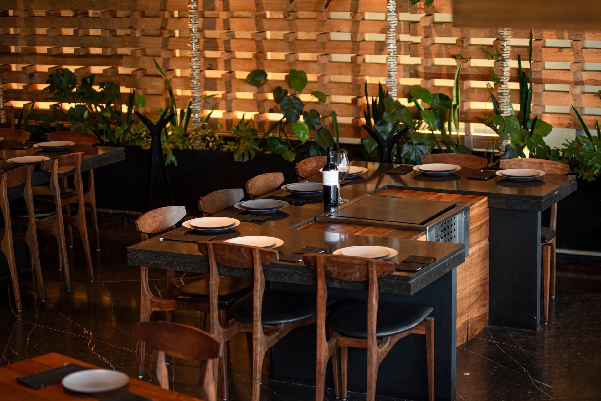 Comedor vacío de un restaurante con mesas de madera, sillas de mimbre e iluminación ambiental cálida.