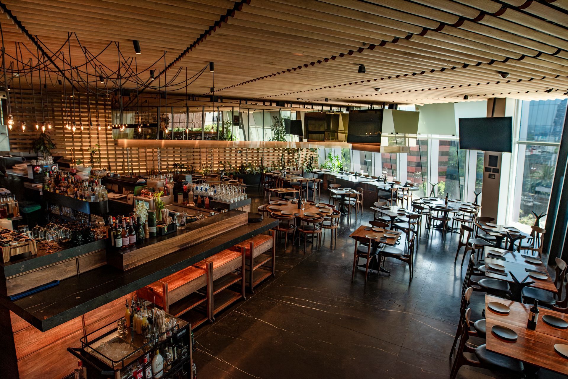 Interior de bar moderno y vacío con mesas, taburetes e iluminación ambiental cálida.