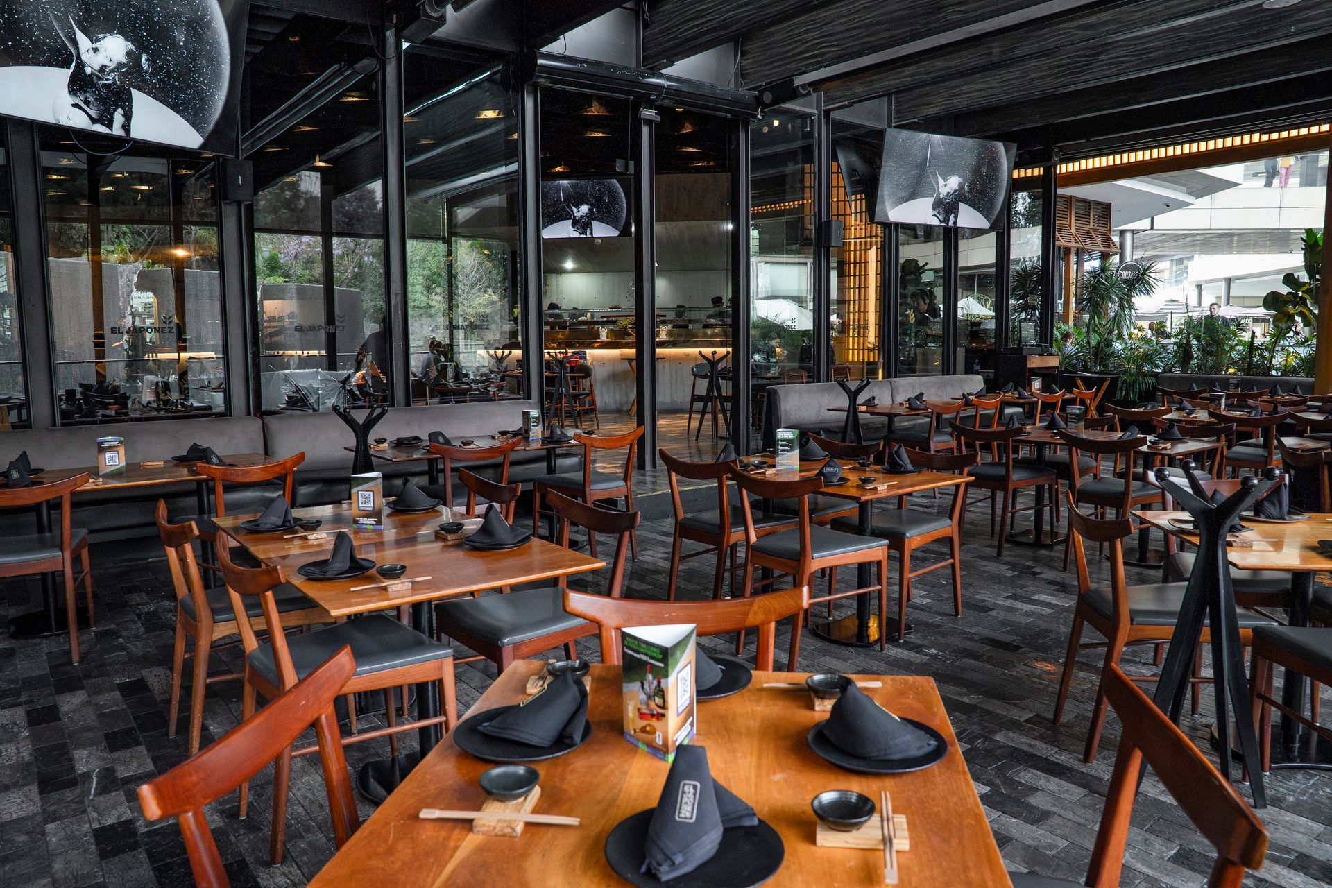 Restaurante al aire libre vacío con mesas y sillas de madera bajo un patio cubierto.