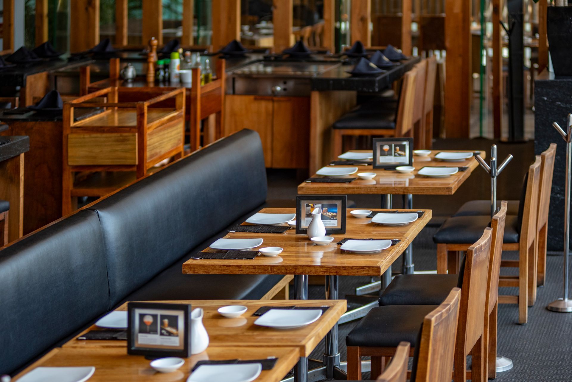 Comedor vacío de un restaurante con mesas de madera, bancos negros y vajilla.