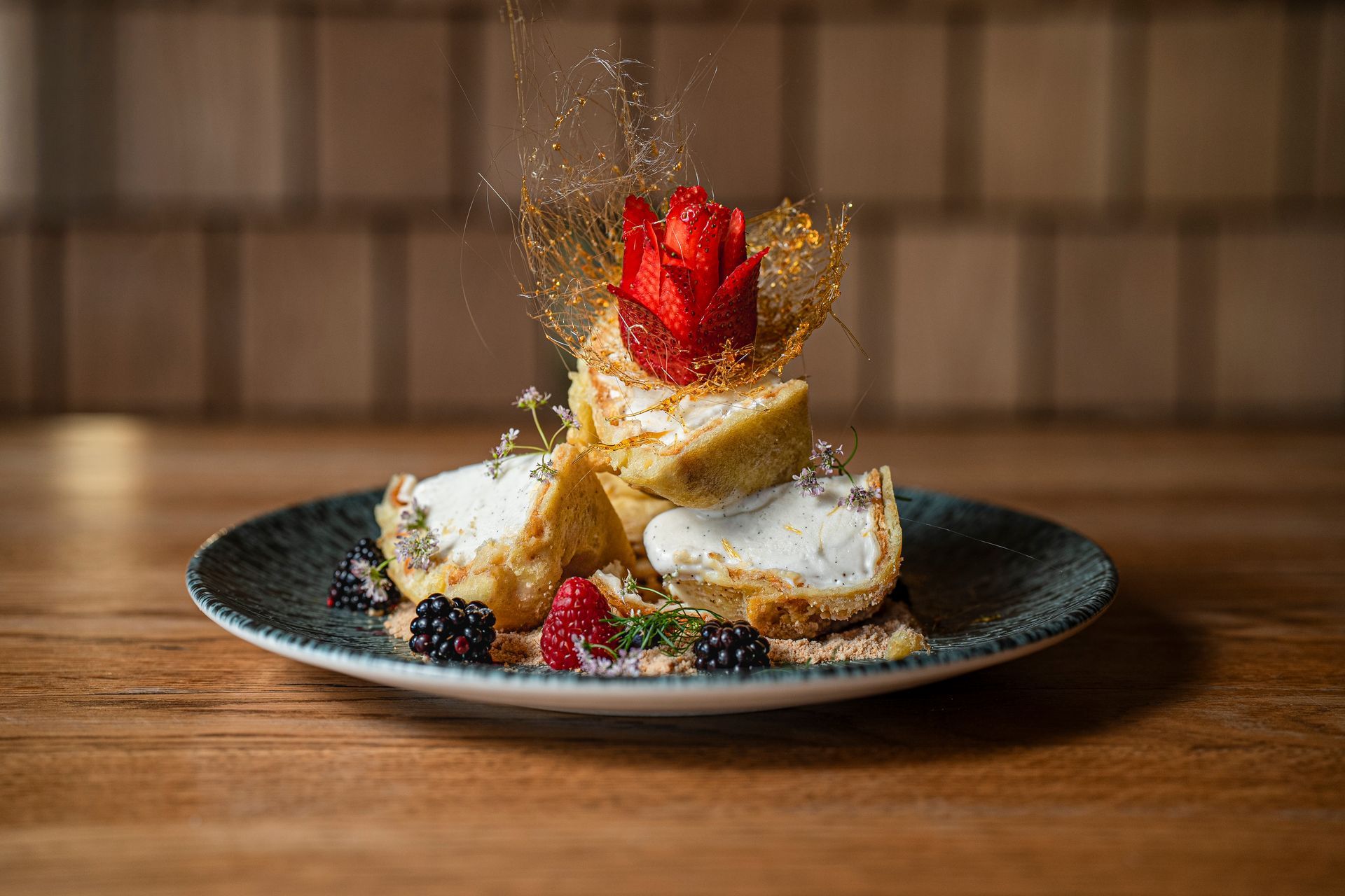 Plato de postre con rebanadas de pastel, frutos rojos, crema batida y una guarnición de fresas sobre una mesa de madera.
