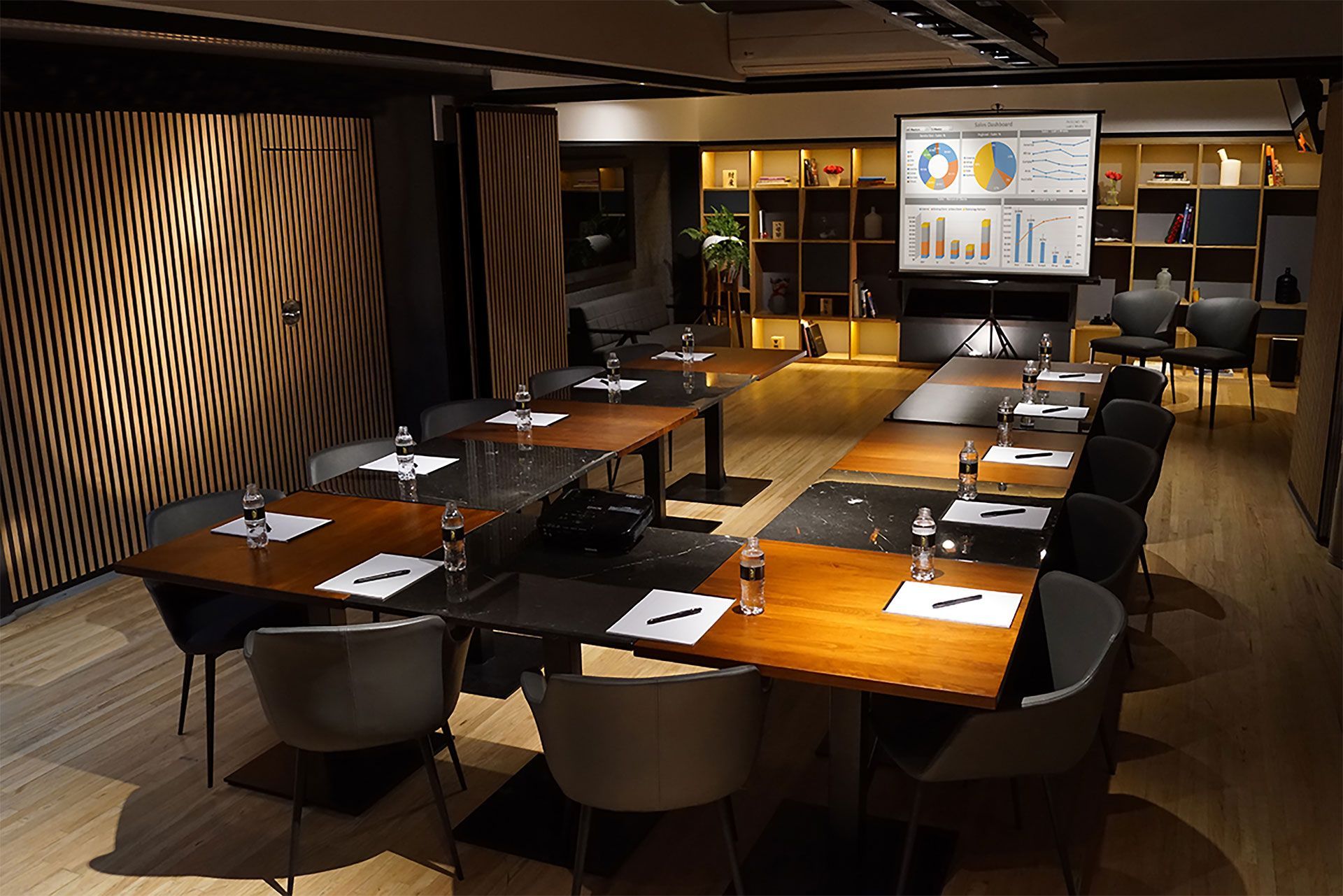 Sala de conferencias moderna y vacía con una gran pantalla de presentación y una larga mesa de madera.