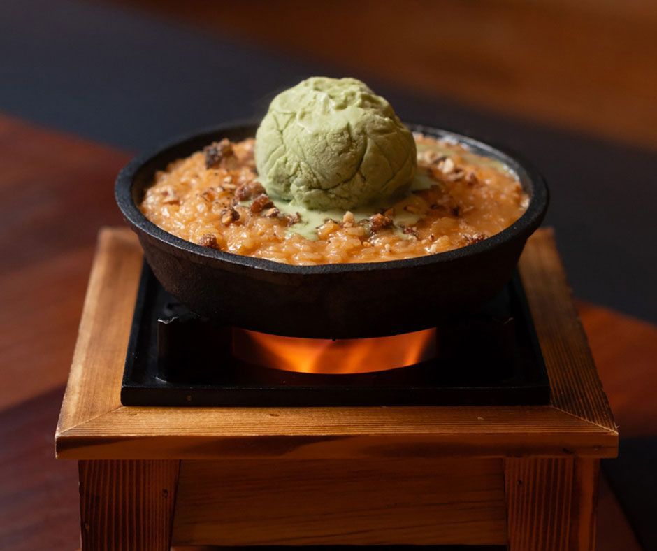 Postre en sartén cubierto con helado verde, servido en un soporte de madera.