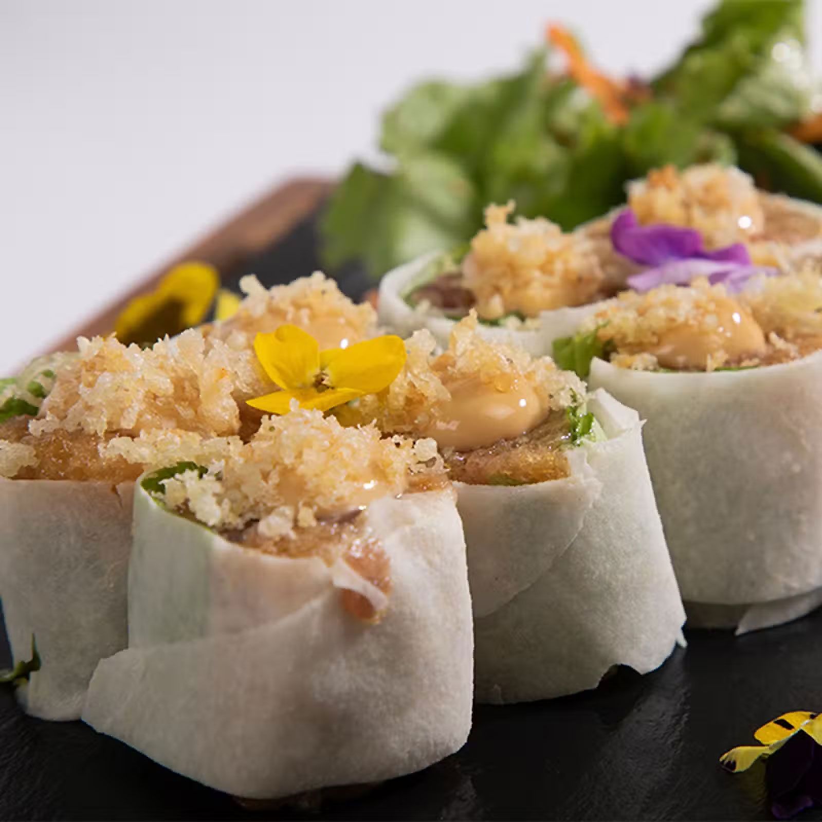 Empanadillas al vapor cubiertas con migas y flores comestibles en un plato negro.