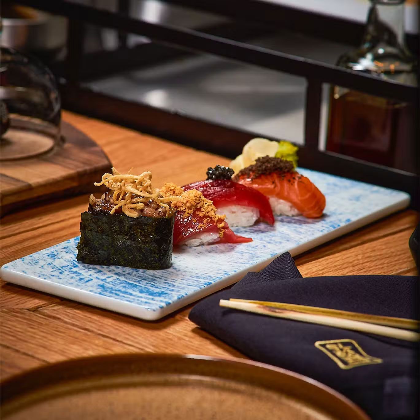 Plato de sushi en un plato azul con palillos y una servilleta doblada sobre una mesa de madera.