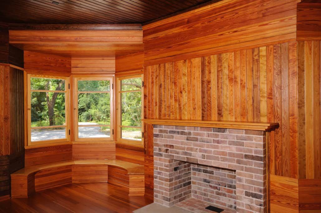 Cozy room with wood paneling, bay window with bench, brick fireplace.