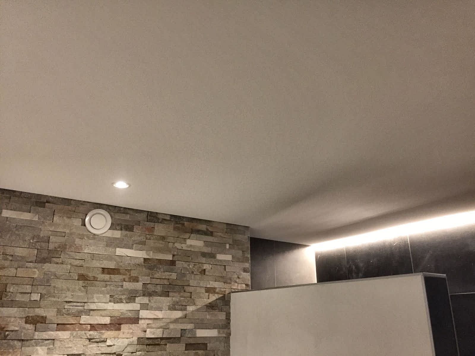 Stenen muur, plafond met inbouwspot en lineaire verlichting.