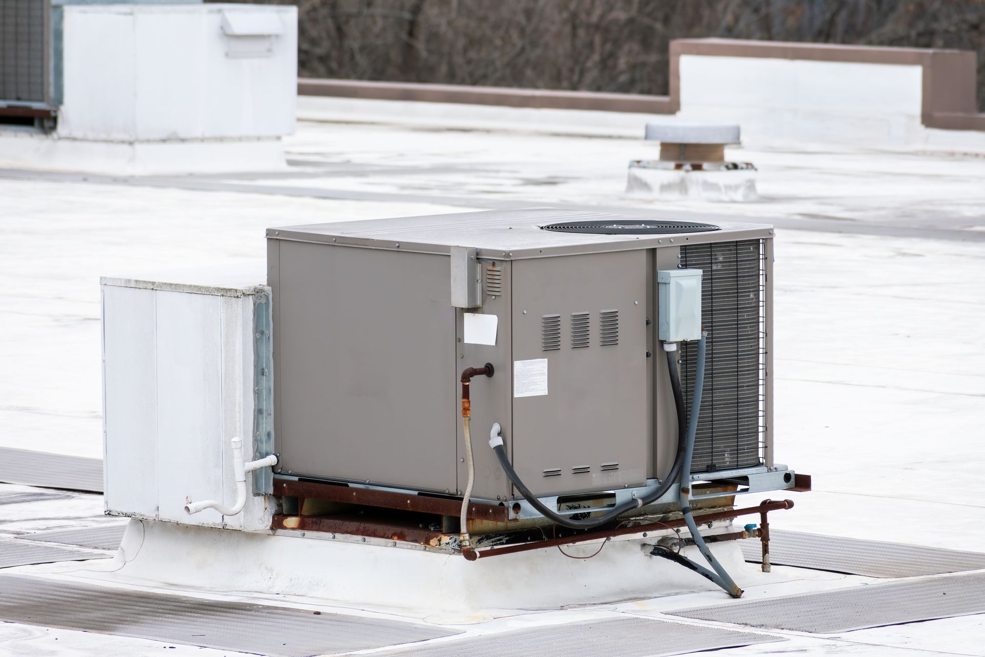 Gray rooftop HVAC unit with exposed wiring on a snowy flat roof