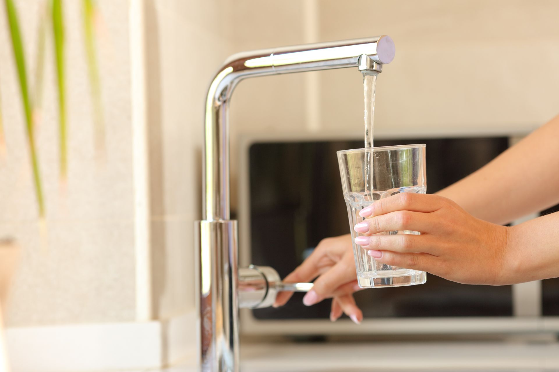 Hand holding a glass under a kitchen faucet as water pours into it