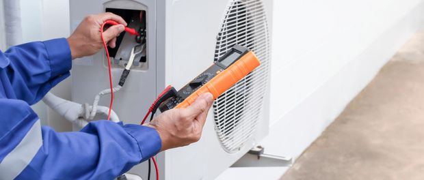 Technician using a multimeter to test an electrical outlet and wall vent