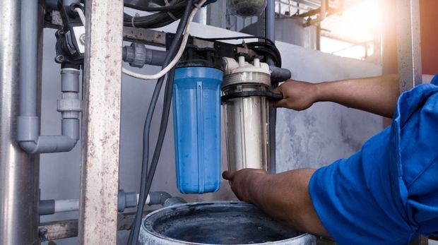 Technician replacing a blue water filter cartridge under a sink.