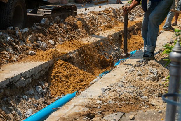 Workers digging a trench beside blue pipes in a muddy construction site