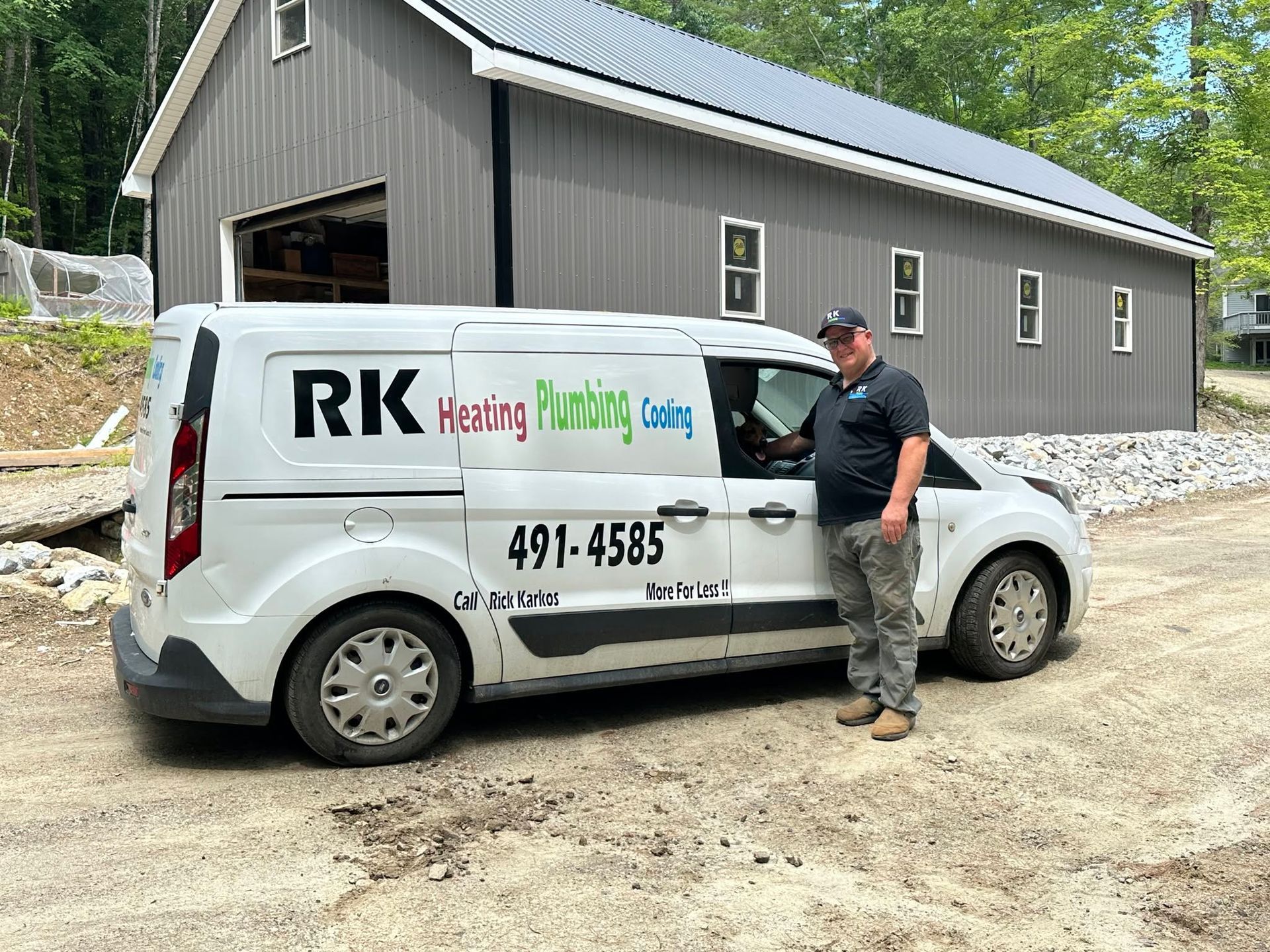 Man leaning on a white RK Heating Plumbing van outside a gray building on a dirt lot