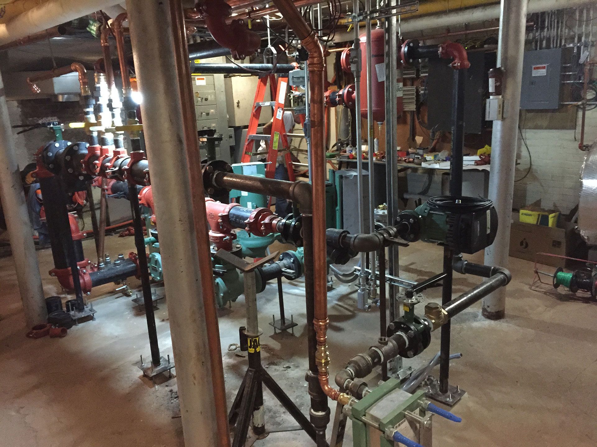 Mechanical room with pipes, valves, and industrial equipment in a dimly lit basement setting