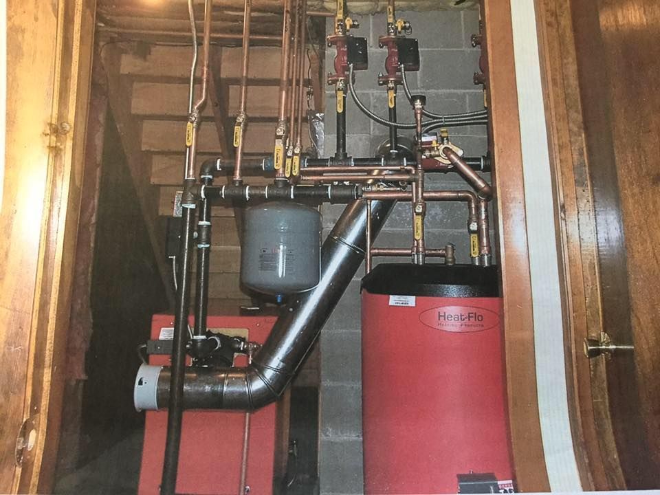 Boiler room with red and gray water heater, pipes, and ducting in a basement alcove