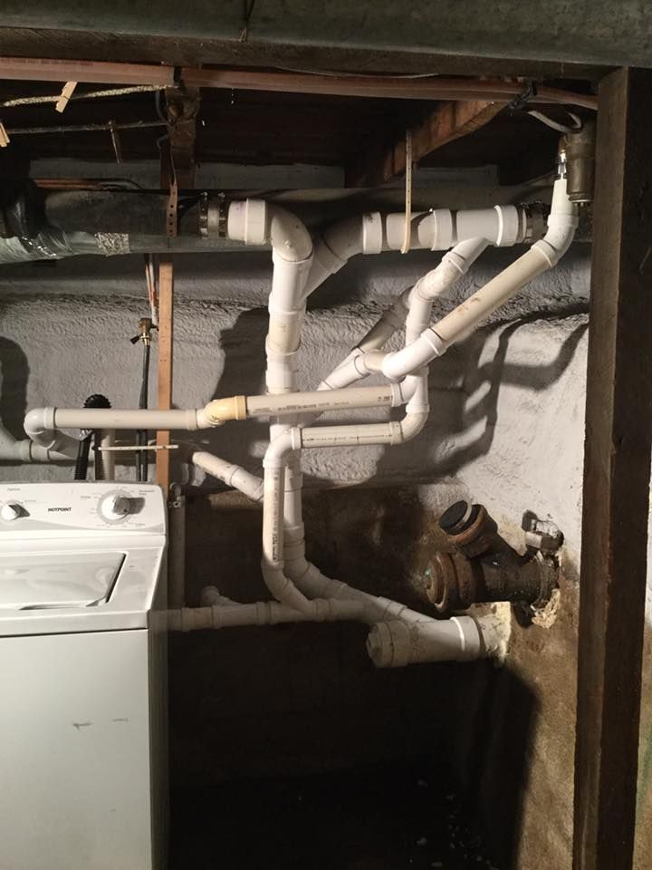 Basement laundry area with exposed white pipes, a washer, and a utility meter on a concrete wall