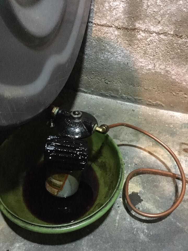 Black cylindrical device in a green bowl with a copper tube beside it on a concrete floor near a wall