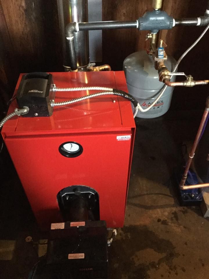 Red boiler furnace in a utility room with silver pipes and a gray tank beside it