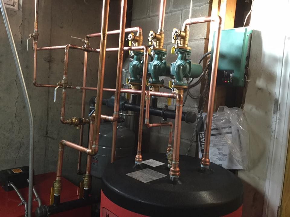 Copper pipe sculpture with teal glass jars mounted on a black base indoors