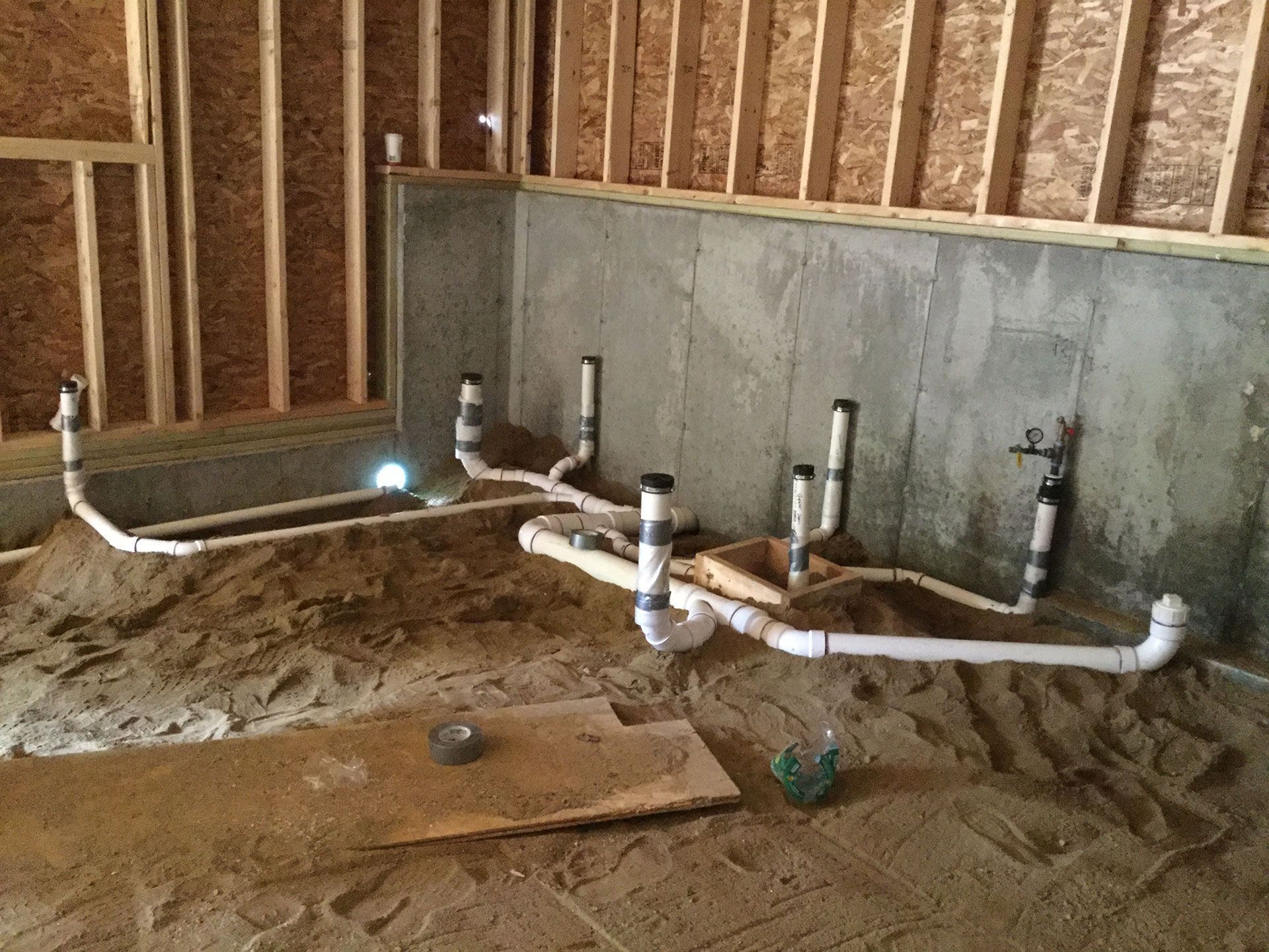 Plumbing rough-in with white pipes and black fittings in an unfinished room with exposed studs.