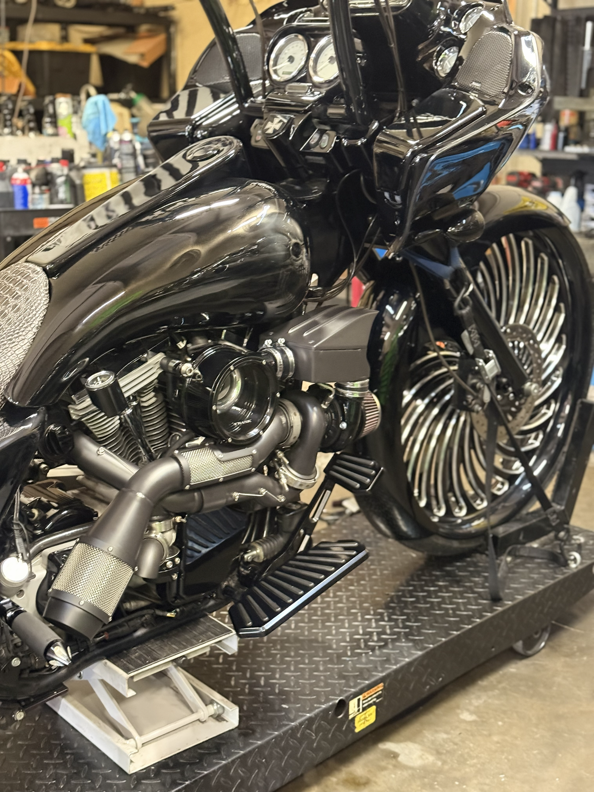 Custom black motorcycle on a workshop lift, with polished chrome engine and oversized front wheel