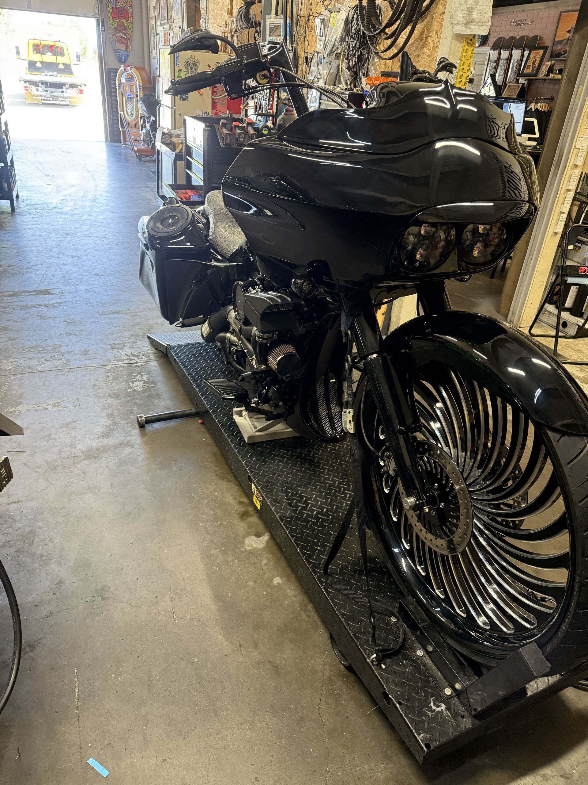 Black custom motorcycle with spoked front wheel on a display platform in a garage or shop。
