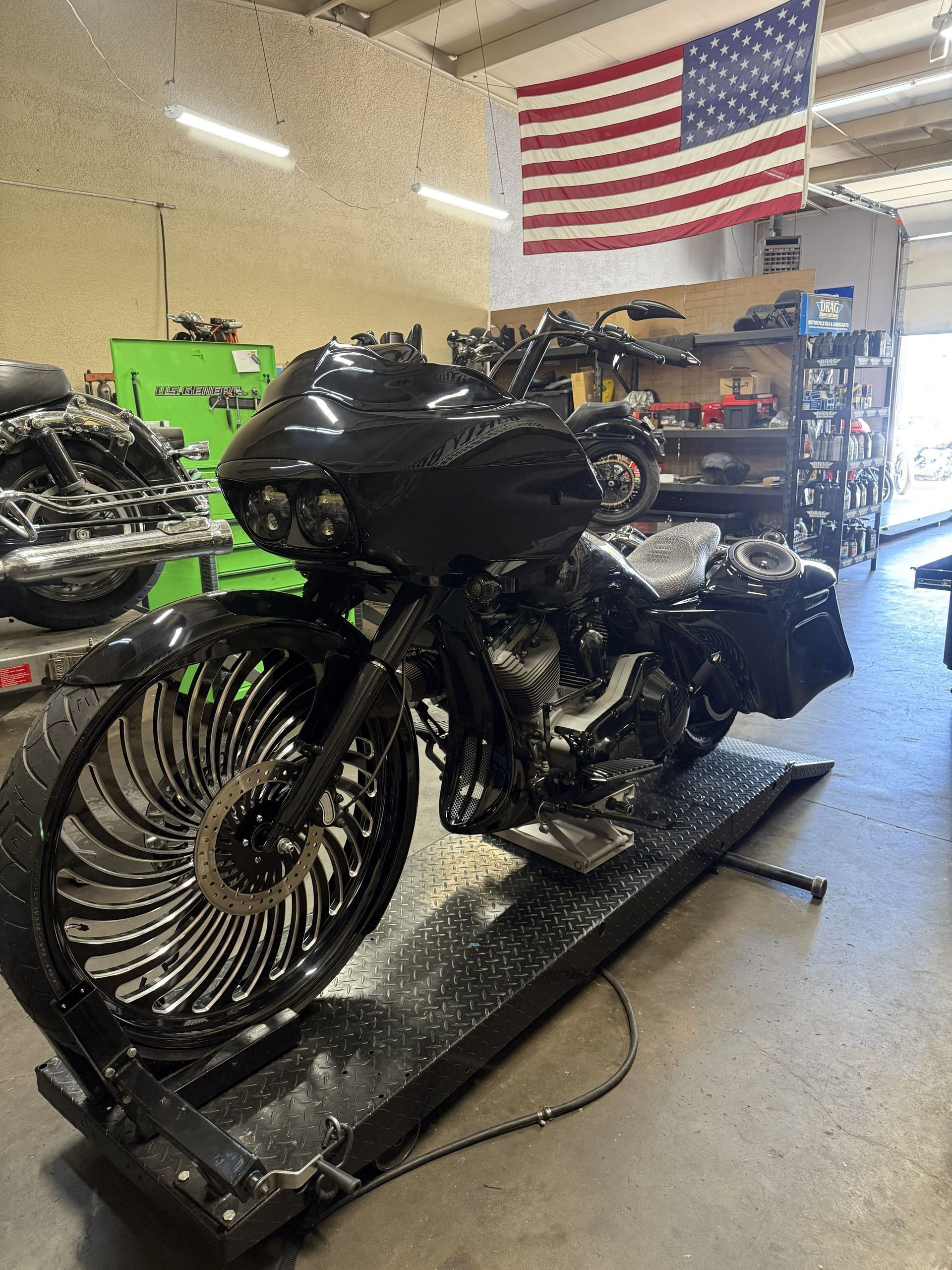 Black custom motorcycle on a lift in a shop with an American flag hanging above