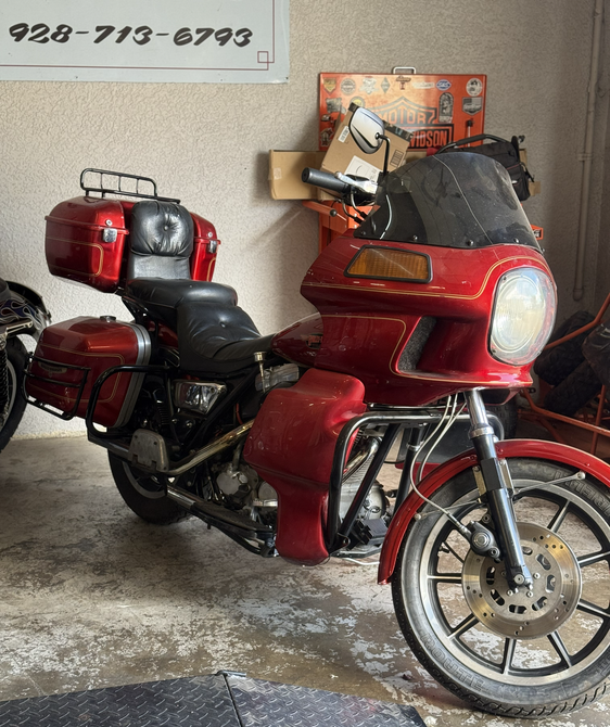 Red touring motorcycle with black seat and top case parked indoors on a concrete floor.