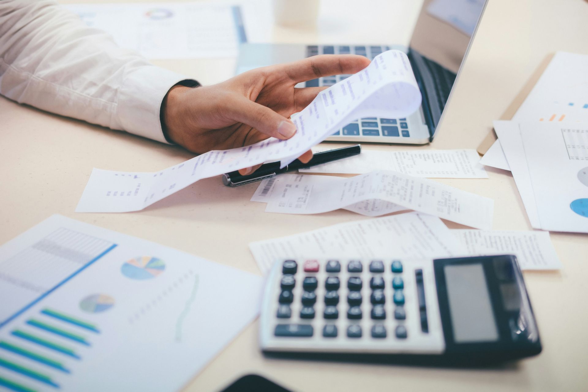 Person reviewing receipts with a calculator, laptop, and financial documents on a desk.