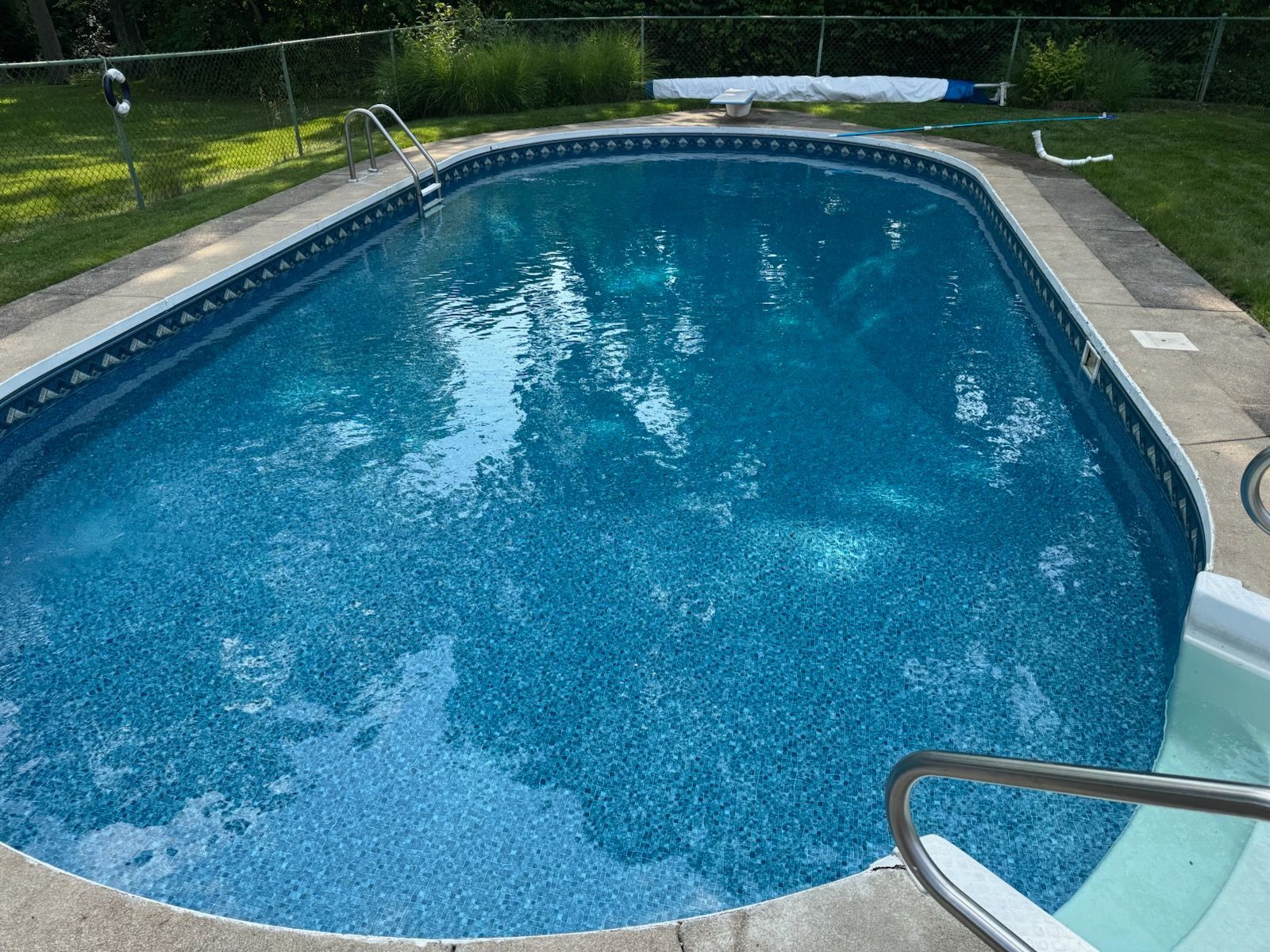 An outdoor rectangular swimming pool with blue speckled lining, surrounding concrete deck, and metal access ladders.