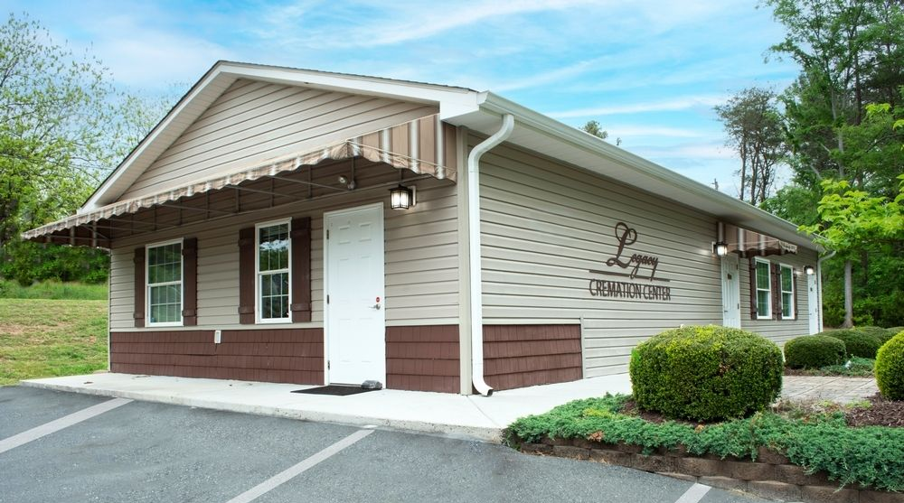 Single-story beige building with white trim, brown lower facade, and a gabled roof beside a parking lot and greenery