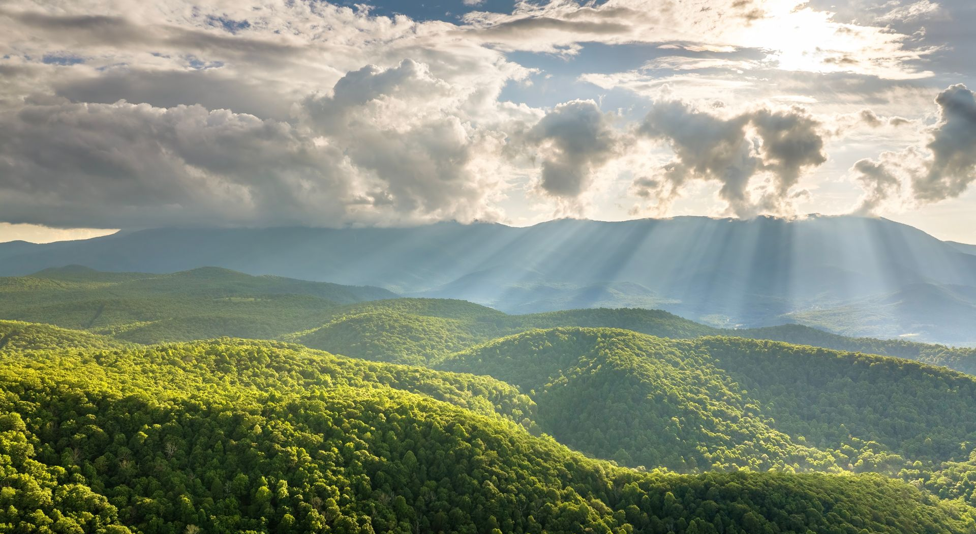 Sunlit green hills beneath a cloudy sky with rays of light streaming through